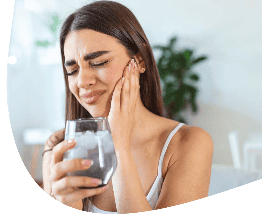 Žena držící sklenici vody se dotýká bolavého zubu, výraz bolesti.